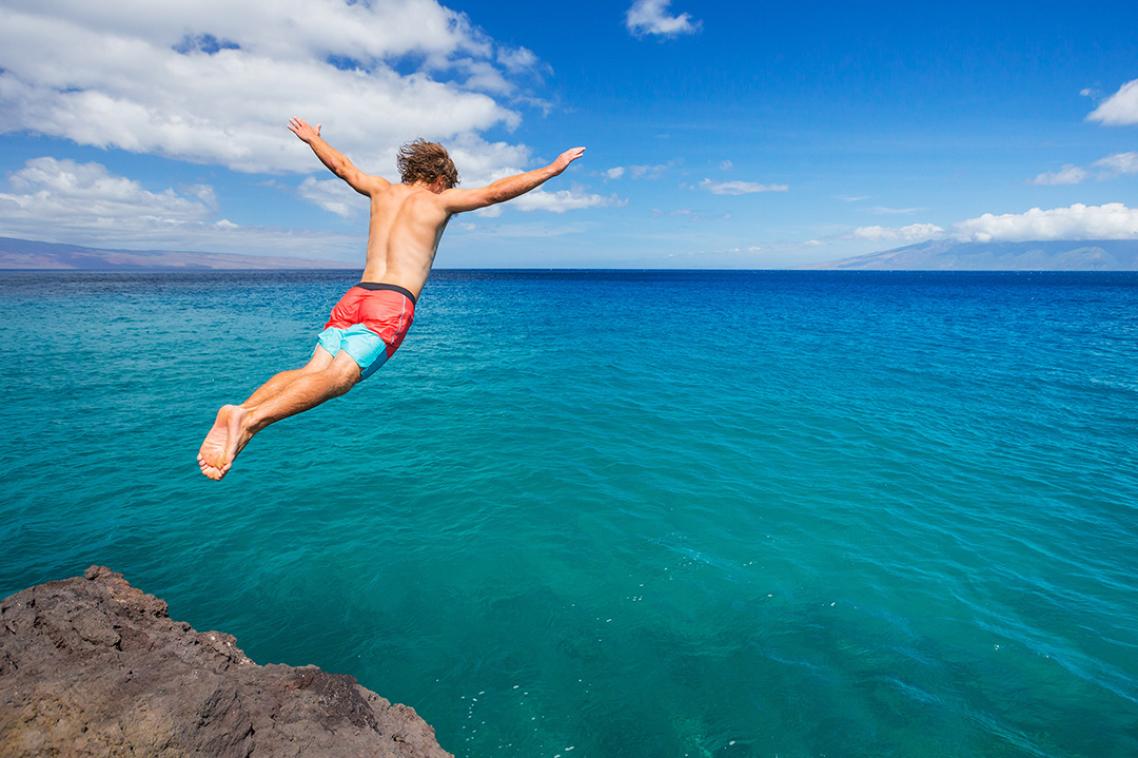 A man diving into the ocean from a cliff.