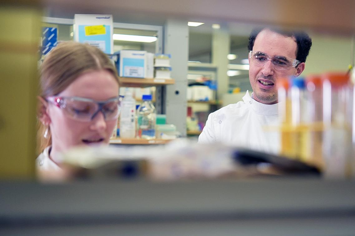 Two scientists – a woman and a man – working at a work station in a science lab.